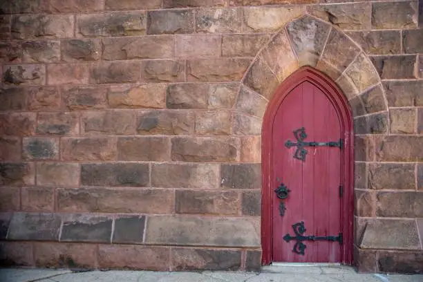 Photo of Old red church door off center in brown stone exterior wall