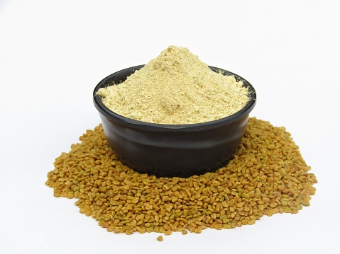 Fenugreek powder in a bowl with seeds isolated on white background