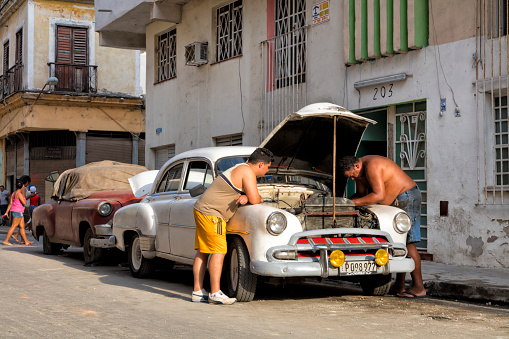 Havana, Cuba - April 20, 2016: Cuban men peek into the engine of an old American car in as they perform maintenance on the street.