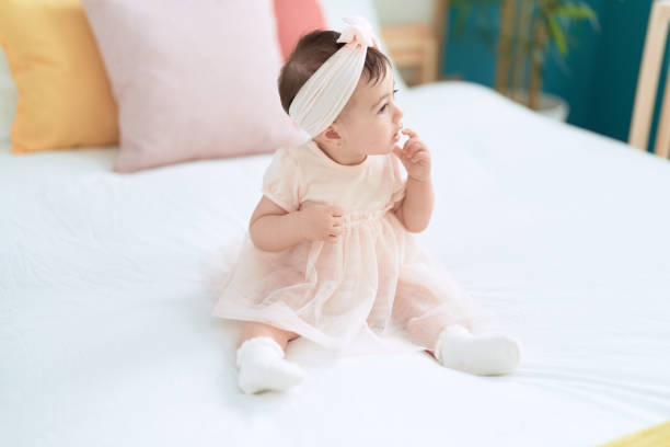 Adorable toddler sitting on bed with relaxed expression at bedroom