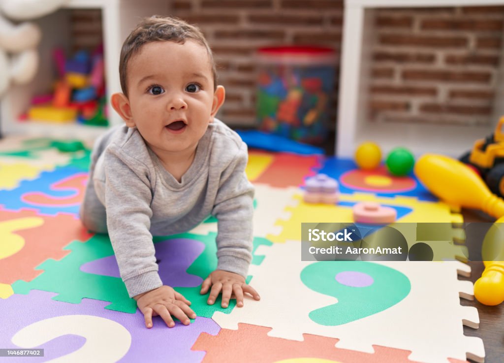 Adorable hispanic baby crawling on floor at kindergarten Baby - Human Age Stock Photo