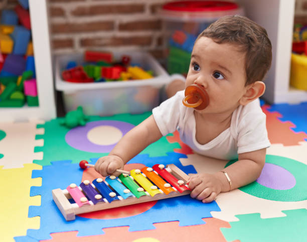 istock Adorable hispanic baby playing xylophone lying on floor at kindergarten 1446877444