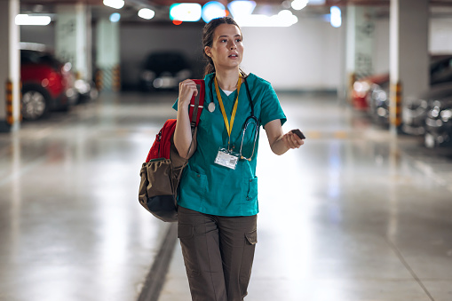 A young Caucasian female nurse is walking around an underground garage searching for her car.