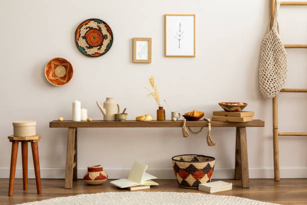 istock Creative composition of elegant and boho living room with wooden bench, side table, hanging decoration, bamboo ladder, books, baskets, mock up photo frames and personal accessories. Cozy home decor. 1446878086