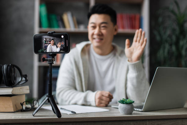 istock Attractive asian man in casual clothes talking and gesturing while recording video on modern phone 1446878658
