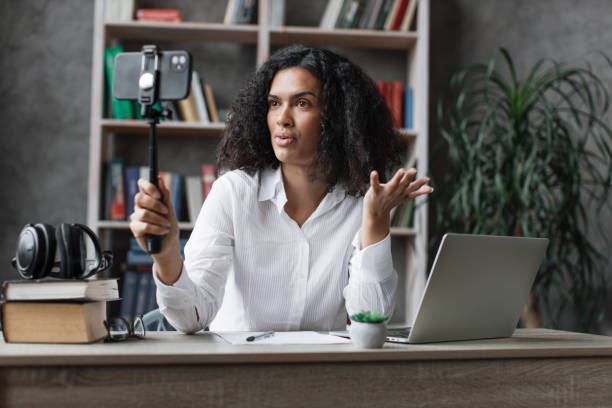 istock Charming multinational woman recording video on modern phone on stick. 1446878715