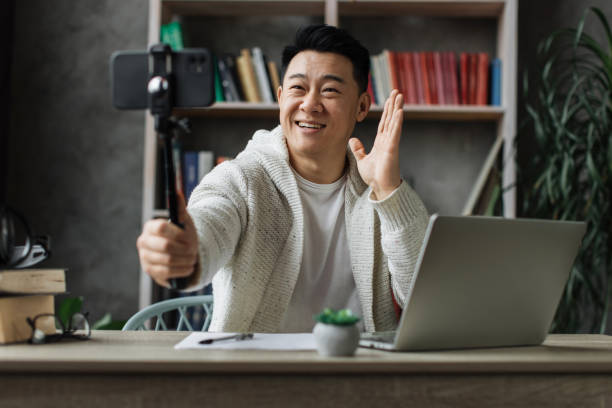 istock Handsome young asian man recording video on modern phone on stick 1446878731