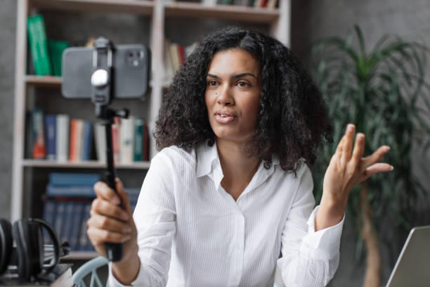 istock Attractive young multinational woman in white shirt taking selfie on her smart phone using stick. 1446878749