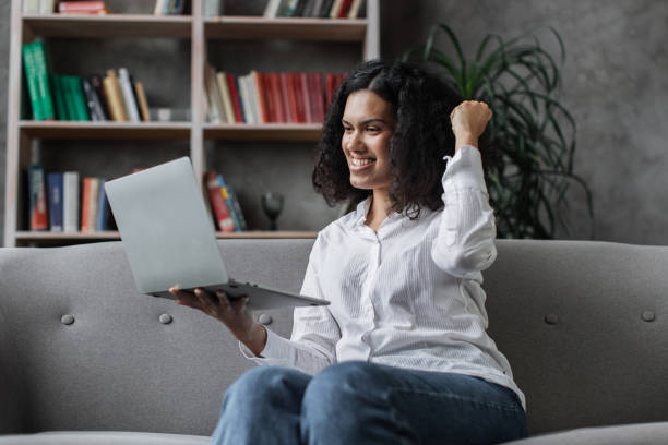 istock Surprised multiracial female sitting on couch and gesturing from happiness while reading good news 1446878780