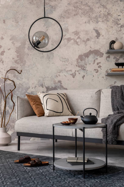 istock Exquisite and modern composition of living room interior with design grey sofa, rug, round pedant lamp, black coffee table, decoration, pillow and elegant accessories. Concrete grunge wall. 1446880774