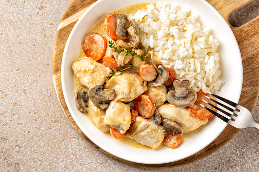 Closeup of Blanquette de poulet, French chicken stew with carrots, mushrooms, onion. Simmered in a white stock and served in a sauce enriched with cream,  with white rice in a white plate.