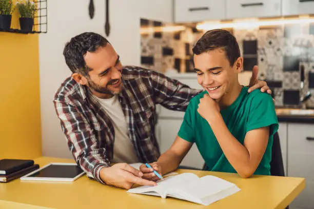 Father is helping his son with learning. They are doing homework together.