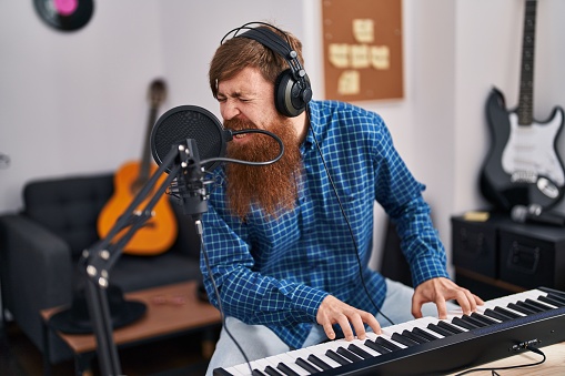 Young redhead man musician singing song playing piano at music studio