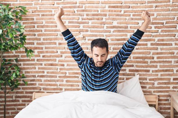 istock Young hispanic man waking up stretching arms at bedroom 1446884264