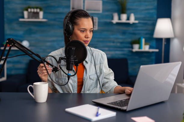 istock Woman vlogger streaming podcast and using laptop at desk. 1446884468