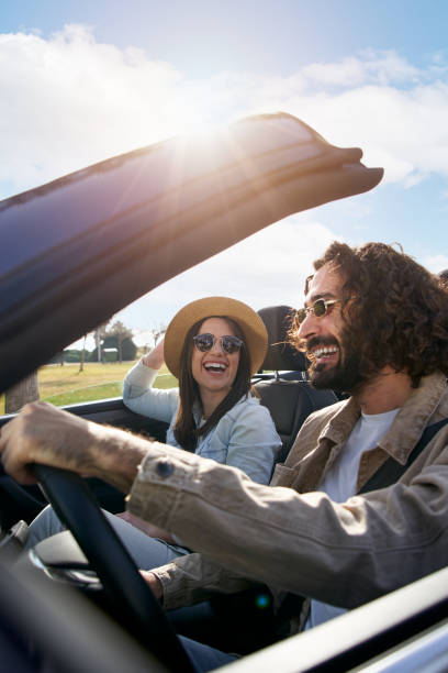 A young cheerful Caucasian couple driving in a convertible car enjoying the freedom of weekend trip stock photo