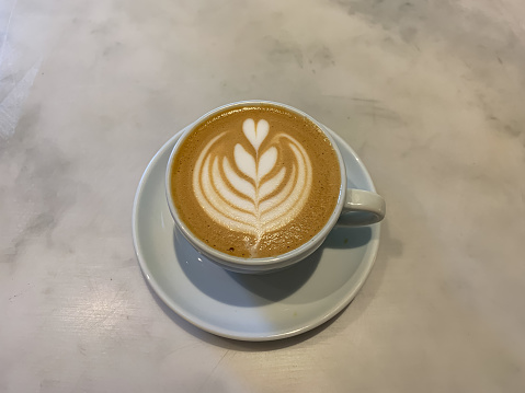 A mug of flat white coffee on a marble background. Coffee art. Heart flower shape latte art. Copy space