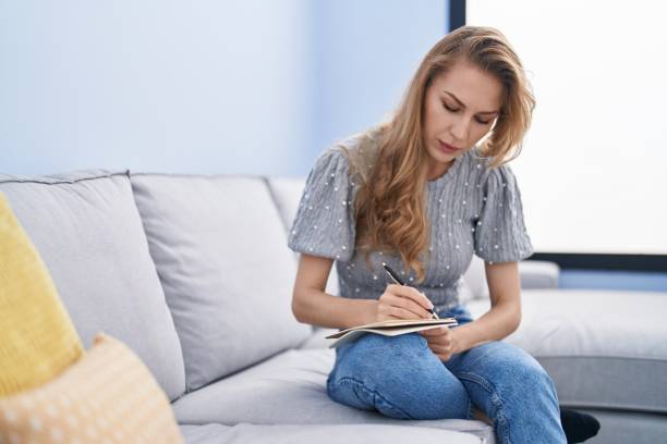 istock Young blonde woman writing on notebook sitting on sofa at home 1446885601