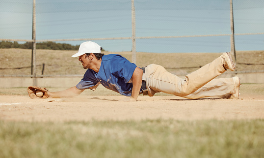 Sports, action and a man catching baseball, sliding in dust on floor with ball in baseball glove. Slide, dive and catch, baseball player on the ground during game, professional athlete on the field.