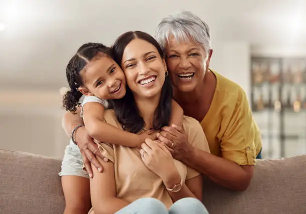 Photo of Grandmother, mom and child hug in a portrait for mothers day on a house sofa as a happy family in Colombia. Smile, mama and elderly woman love hugging young girl or kid and enjoying quality time