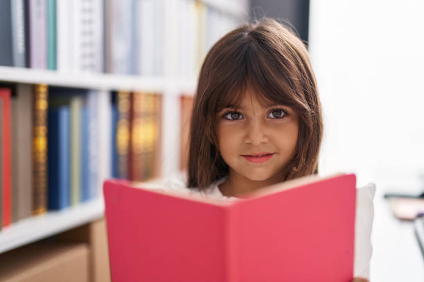 Adorable hispanic girl student smiling confident reading book at classroom