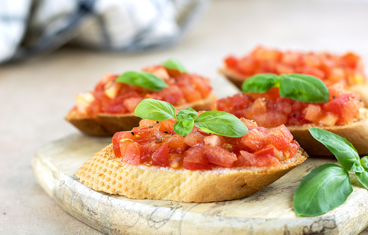 Bruschetta or crostini made with fresh tomatoes, olive oil and basil on a gray background. Selective focus. Traditional Italian appetizers.