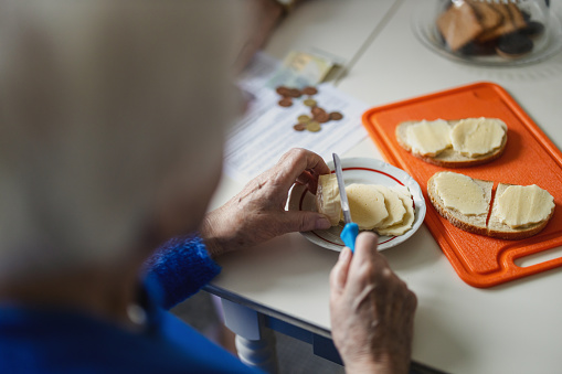 Close-up of the hands of an elderly woman making sandwiches in the kitchen