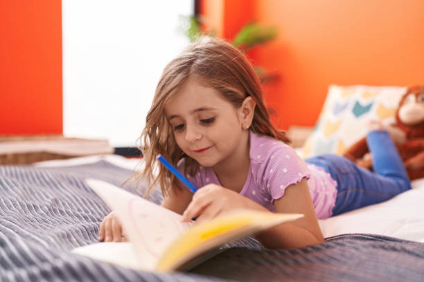 istock Adorable hispanic girl writing on notebook lying on bed at bedroom 1446888440