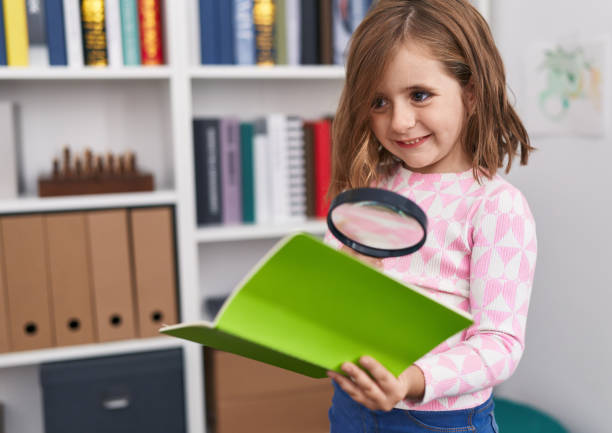 istock Adorable hispanic girl student reading book using magnifying glass at library school 1446888479