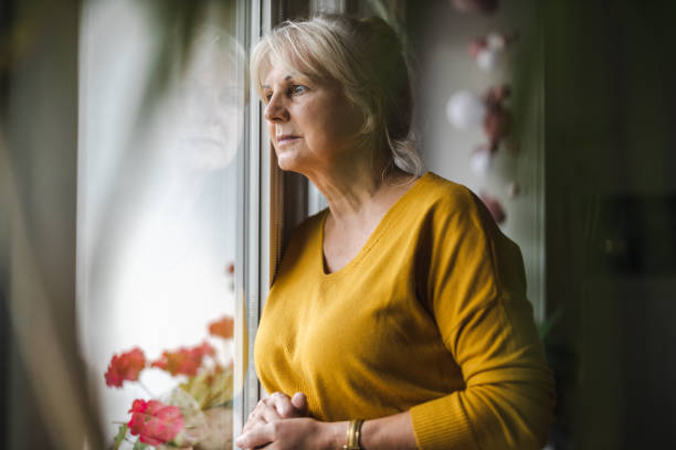 femme âgée inquiète regardant par la fenêtre - women depression window sadness photos et images de collection
