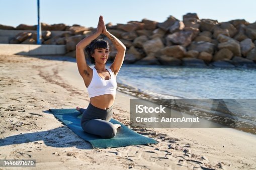 istock Young woman training yoga exercise sitting on sand at seaside 1446891670