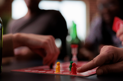 Close up of people hands moving plastic figurines on game table while sitting at table. Group of friends playing boardgames together while enjoying snacks and cold beverages.