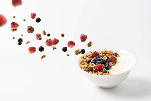 Granola flakes flying in the air with hazelnuts, raspberries, blueberries