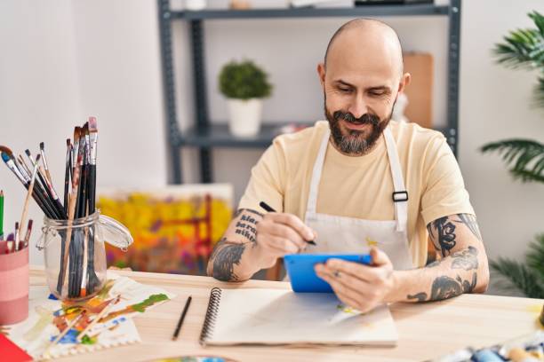 Young bald man artist smiling confident drawing on touchpad at art studio