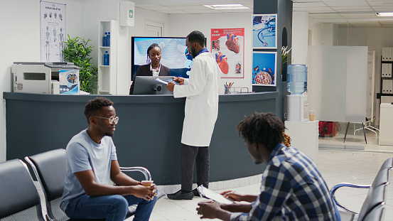 Healthcare experts doing consultations with african american patients, people with disease waiting in hospital lobby area. Group of men sitting in waiting room before attending appointment.