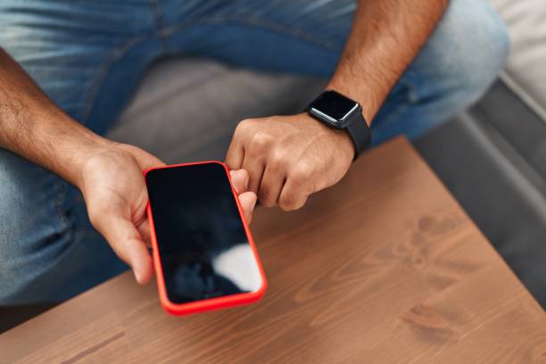 istock Young hispanic man using smartphone and smartwatch at home 1446895516