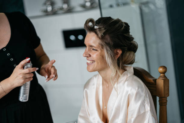 bride getting ready for wedding with stylist using hairspray and curlers