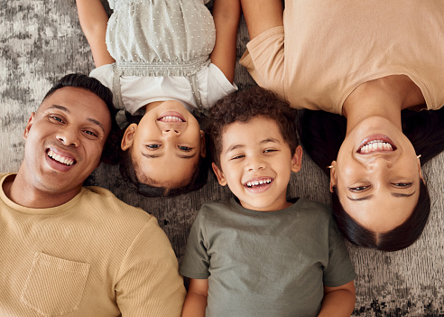 Children, parents and lying on floor from above, happiness spending time together in family home. Mom, dad and young kids smiling on carpet, happy home Brazil for future fun and laughing on weekend.