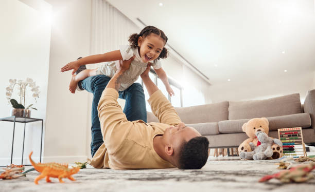 familia feliz, padre y niña jugando en una casa con libertad, uniéndose y disfrutando de tiempo de calidad juntos. felicidad, sonrisa y niño volando en brazos de papá en el suelo en un fin de semana en casa en portugal - monoparental fotografías e imágenes de stock