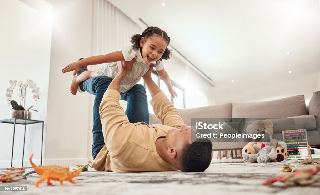 Happy family, father and girl playing in a house with freedom, bonding and enjoying quality time together. Happiness, smile and child flying in dads arms on the floor on a weekend at home in Portugal Child Stock Photo