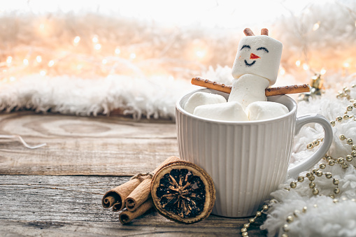 Close up, mug of hot drink with marshmallow snowman on blurred background, copy space.