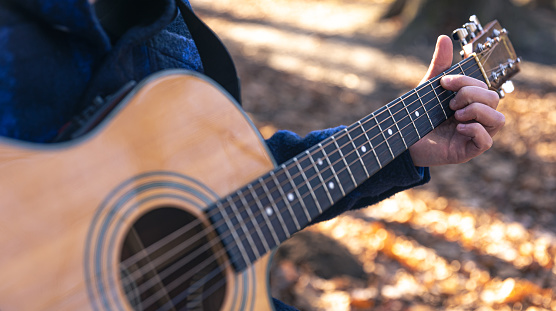 Close-up, a man plays an acoustic guitar in the forest during the cold season.