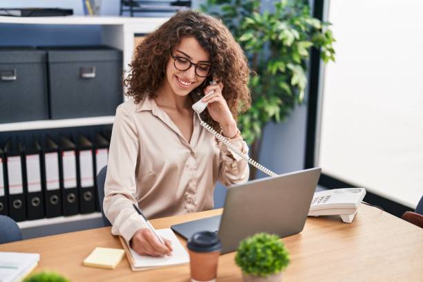 istock Young hispanic woman business worker talking on telephone writing on notebook at office 1446900927