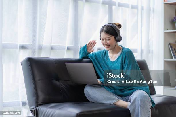 Young Asian Woman Listening To Music On The Sofa In The Living Room At Home Happy Woman Using Laptop To Video Call With Friends On Vacation Stock Photo - Download Image Now