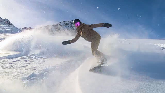 Snowboarder riding down the slope on a majestic powder snow day