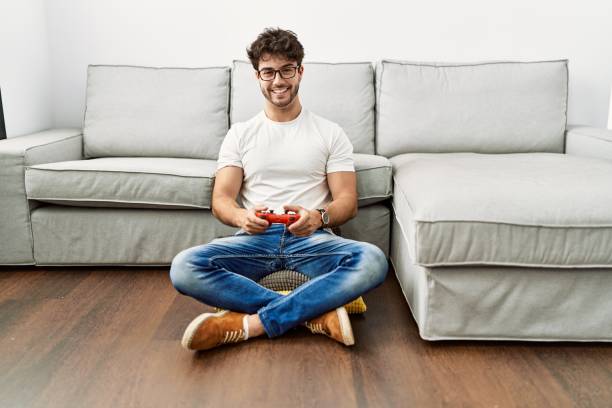 istock Hispanic man playing video game holding controller by the sofa looking positive and happy standing and smiling with a confident smile showing teeth 1446902656