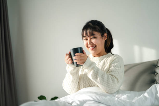 istock Young woman drinking coffee in bedroom, Holding coffee cup with two hands 1446904115