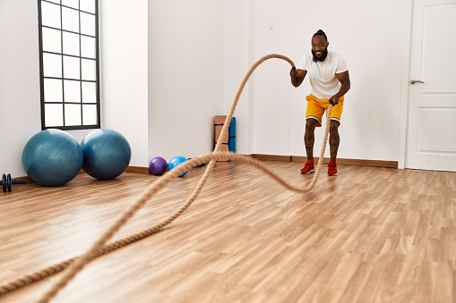 Young african american man smiling confident training with battle rope at sport center
