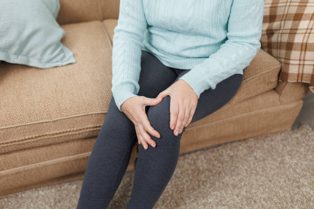 istock Mature woman suffering from knee ache on sofa 1446906792