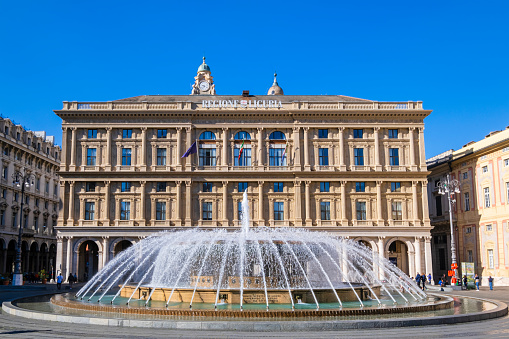 Tourists visiting Piazza De Ferrari in Genoa, the main city square characterized by a large circular fountain and many historic buildings, such as the Palazzo della Regione